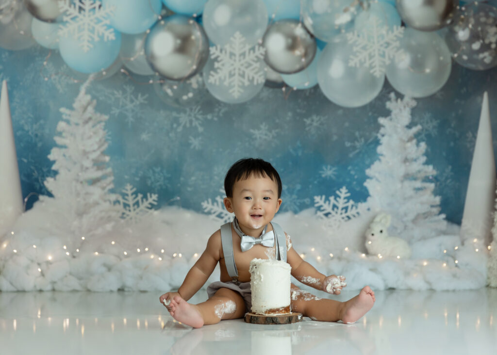 baby boy smiling with his first birthday cake on a a winter wonderland background.