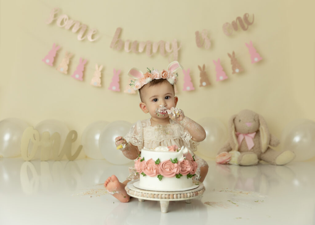 First birthday girl on a cream background for some bunny is one themed eating cake for her birthday photos.