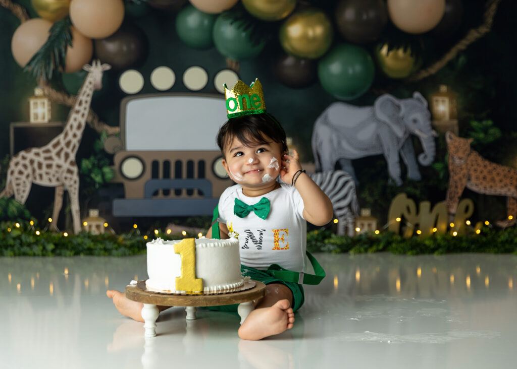 1st birthday boy on a safari themed background smiling with his smash cake.