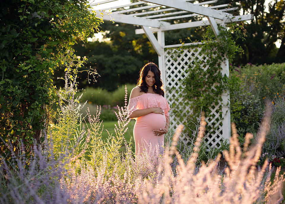 Expecting mother to be wearing a pink maternity dressing standing by purple flowers in an NJ park.