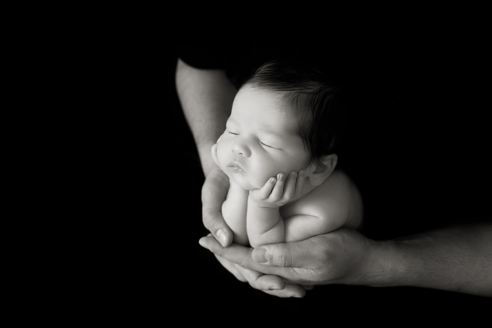 black & white image of a newborn baby boy in dads harnds.