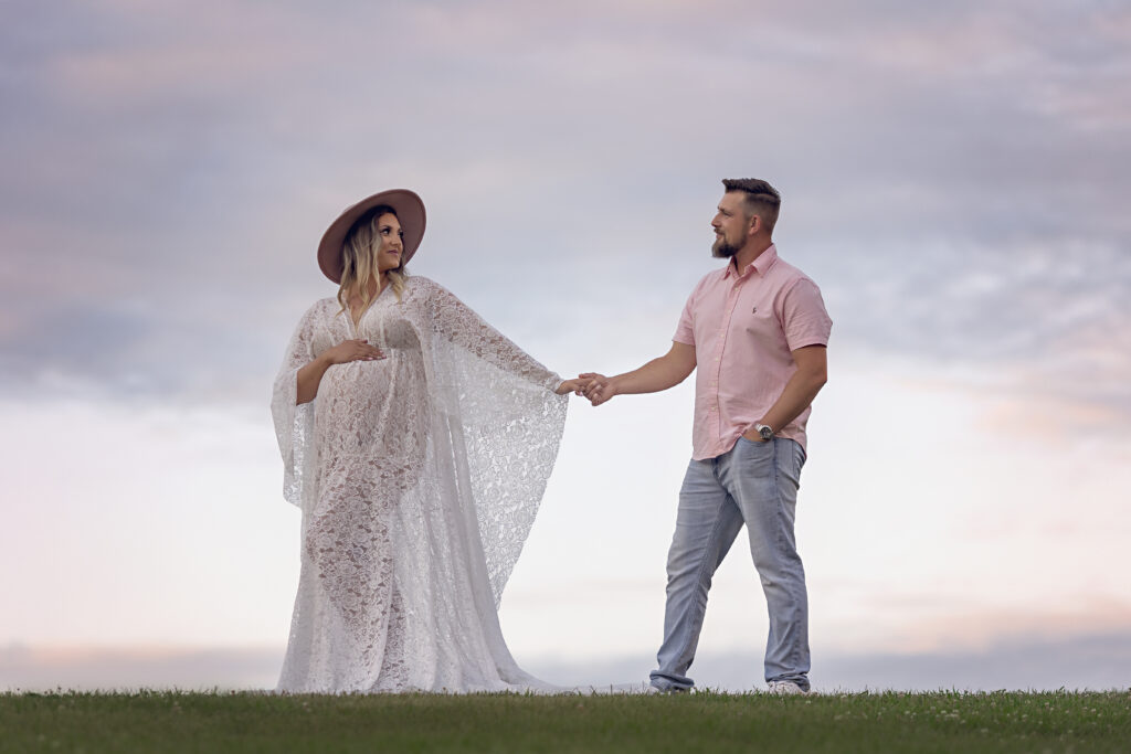 Expecting mother to be wearing a boho dress with her husband holding hands walking in a park at sunset.