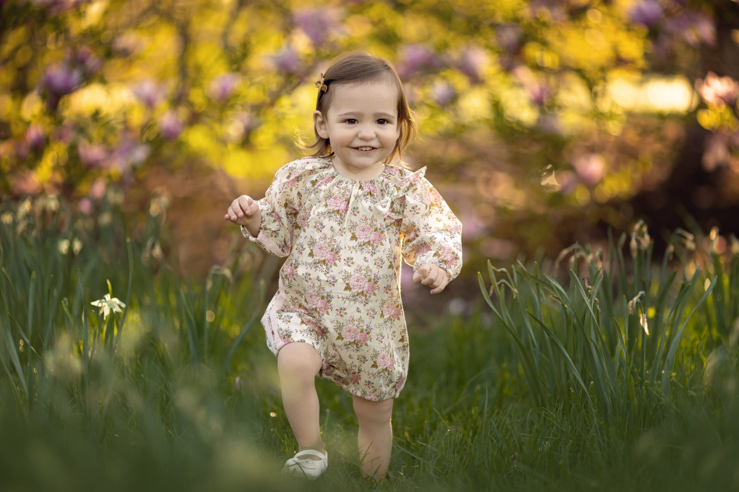 Toddler girl in floral romper walking through tall grass in an NJ park