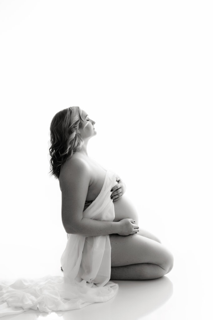 Mother to be draped in white fabric sitting on a background.