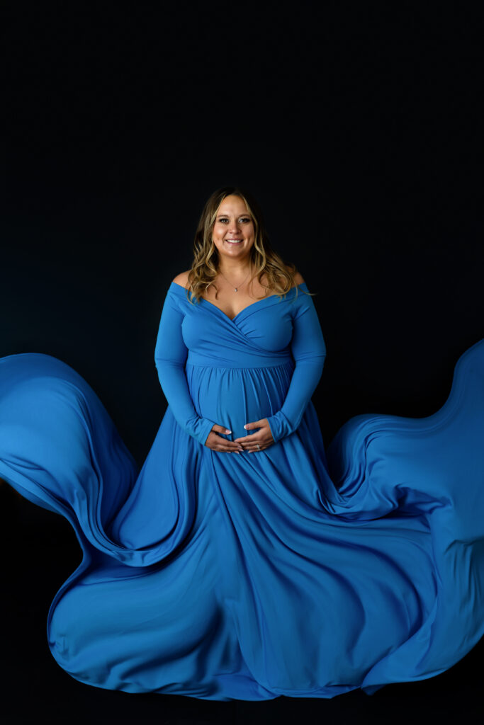 Mother to be in a flowy blue gown on a black background.