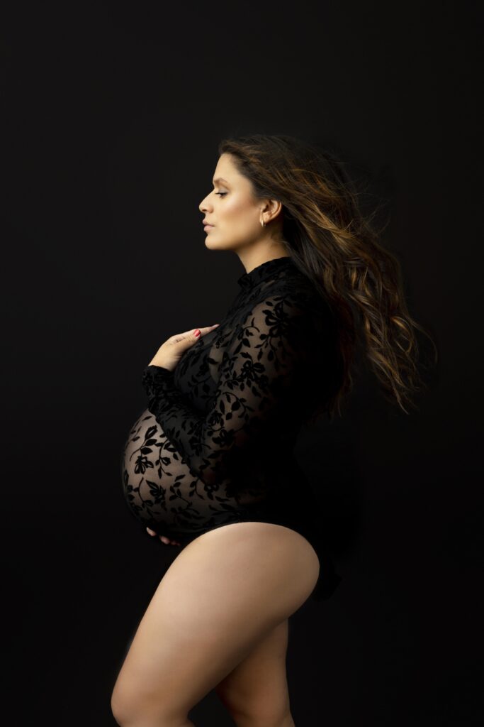 Expecting mother to be in a black lace bodysuit on a black background.