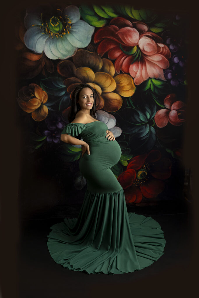 Pregnant mother in a green dress taking maternity photos on a floral background.