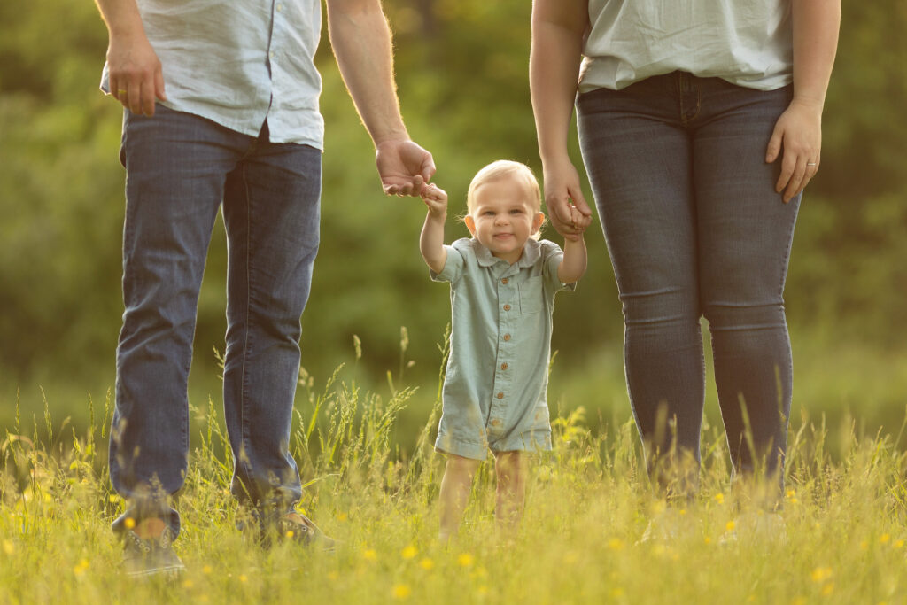 1st birthday boy holding hands with mom & dad in a nj park