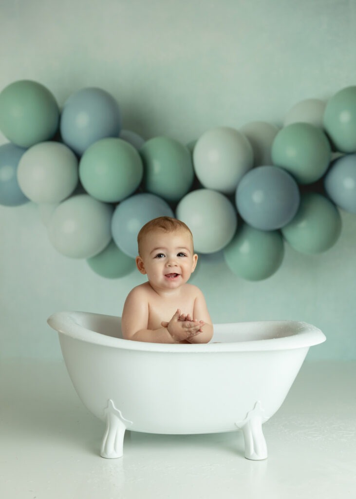 Baby boy in a small bath on a great background with balloon arch after his cake smash session in NJ